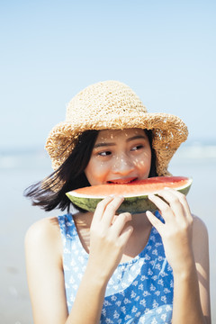 可爱的黑发女孩在沙滩上刮风吃西瓜。