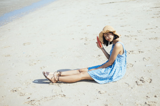 带着西瓜坐在海滩上微笑的可爱女孩。