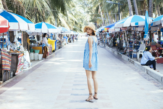 穿着蓝色衣服的可爱女孩在海滩上的市场上散步。