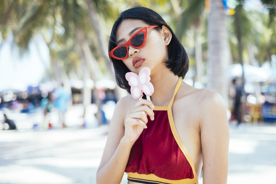 穿着红色短上衣的性感女孩站在海滩上，手里拿着粉色蝴蝶冰淇淋。