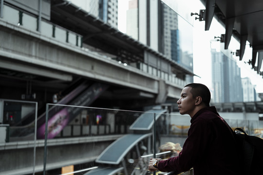 身穿红衫的光头男子站在玻璃路障前，看着对面。