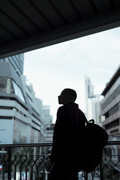 清晨，身穿红衫的光头男子走在天桥上，走进他的办公室，剪影拍摄。