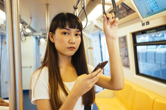 可爱的亚洲年轻女子在火车转向架上玩挂在把手上的手机。