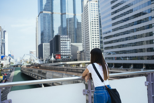 这位年轻的女士靠着扶手独自旅行，眺望着这座城市。