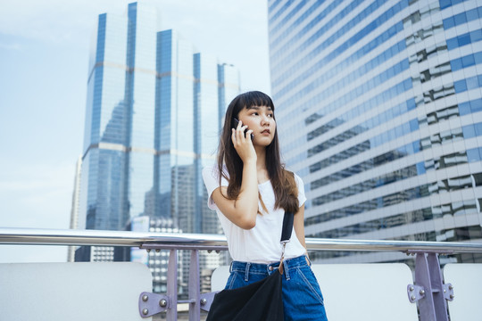 在城市里，一位留着刘海发型的可爱泰国年轻女子在手机上聊天。