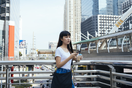 一位留着刘海发型的可爱的亚洲年轻女子，靠在扶手上，手里拿着一杯泡泡茶，用智能手机给她的朋友打电话。