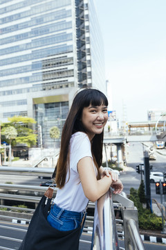 在城市里，一个可爱的亚洲时髦女人靠在扶手上。曼谷年轻女旅行者的时尚肖像。