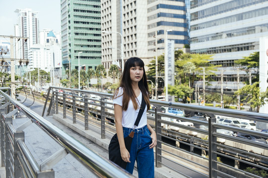 穿着白色衬衫和蓝色牛仔裤的旅行者年轻女子自信地走在天桥上。