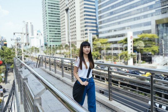 穿着白色衬衫和蓝色牛仔裤的旅行者年轻女子自信地走在天桥上。