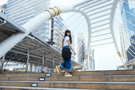 在大城市里，可爱的年轻亚洲时髦女人走上楼梯。