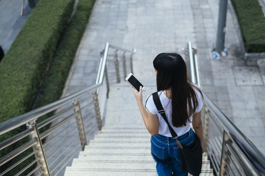 在城市里，一位年轻的时髦女人拿着智能手机走下楼梯。