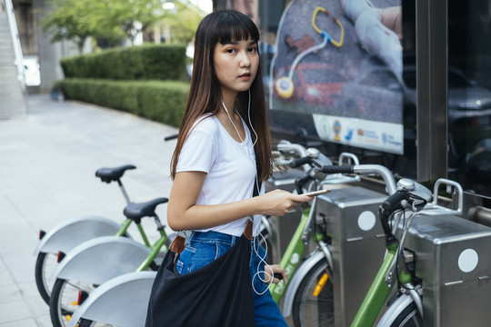 一名年轻的泰国女子戴着耳机听音乐，试图在人行道上骑自行车。