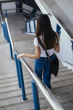 一位身穿白色衬衫和蓝色牛仔裤的匿名年轻女子走下楼梯。