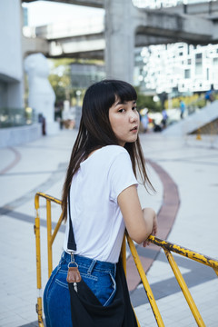 穿着白色衬衫和蓝色牛仔裤，倚在黄色乡村篱笆上的年轻亚洲女性。