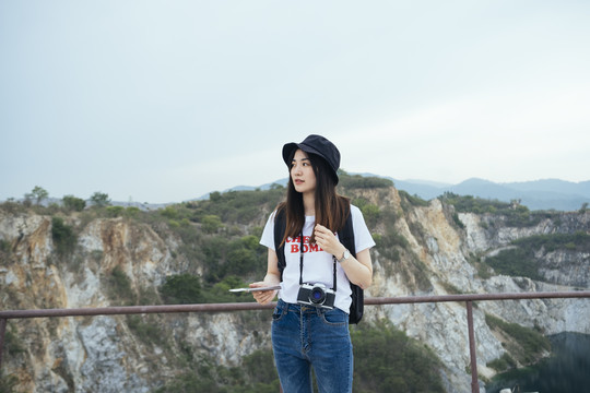 在山区，一位戴着帽子、带着照相机的年轻亚洲长发女旅行者。