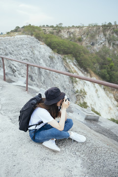 在大峡谷，一位年轻的亚洲-泰国长黑发女游客坐在地板上用相机拍照。春布里。