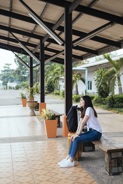 年轻的亚洲长黑发女旅客坐在长凳上，在车站站台等火车。