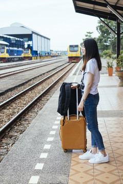 侧视图-年轻的亚泰黑头发旅行家妇女在火车站站台等待火车。