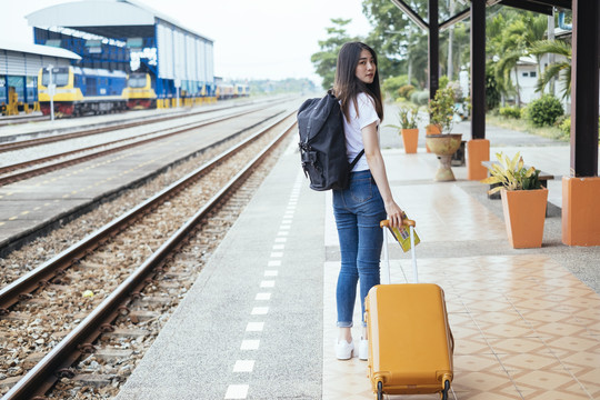 在火车站站台上，一位年轻的亚泰裔黑发旅行家妇女提着手提包行走。
