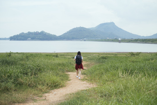 后视图-年轻的亚泰黑头发旅行家女子走进湖中。
