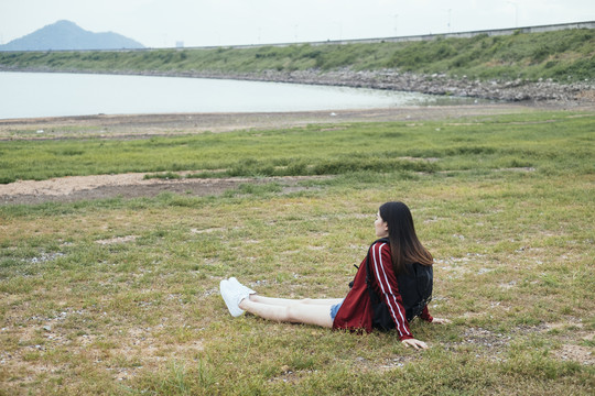 年轻的亚洲泰式长黑发旅行家女子坐在春武里的湖边。