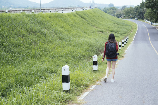 后视图-年轻的亚泰黑头发旅行家妇女走在路上。