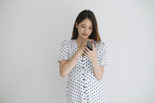 年轻的亚洲女人穿着黑白圆点的衣服，在白色背景下使用手机。在智能手机概念上购物。