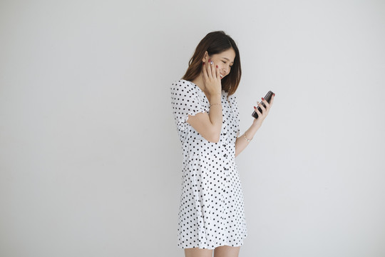 穿着黑白圆点连衣裙的可爱亚洲女人在看到智能手机上的网上购物促销后感到高兴。在白色背景上隔离。
