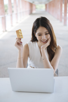 年轻漂亮的亚洲女士用笔记本电脑上的信用卡进行网上购物。