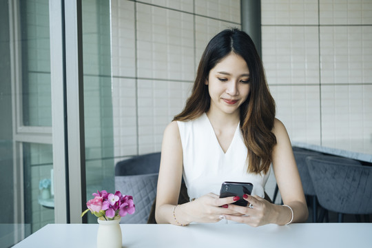 一位穿着白衬衫的亚洲女士用智能手机和她的朋友聊天。