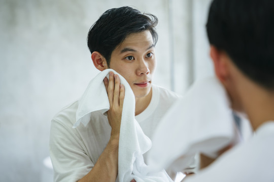 亚洲年轻人在浴室用毛巾洗脸。