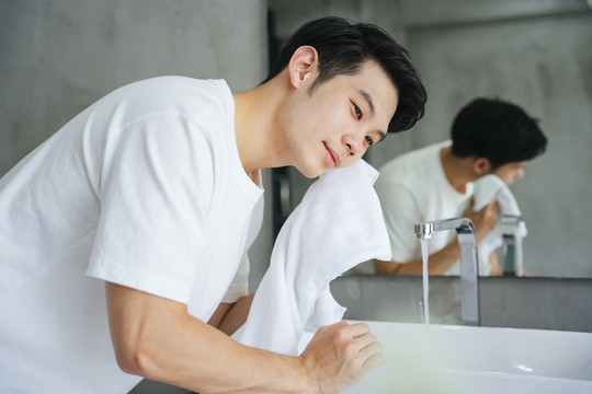 亚洲年轻人在浴室用毛巾洗脸。