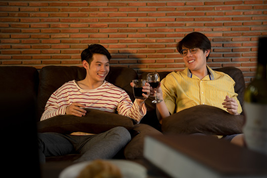 一对亚洲LGBTQ+男士在家用葡萄酒庆祝结婚周年。