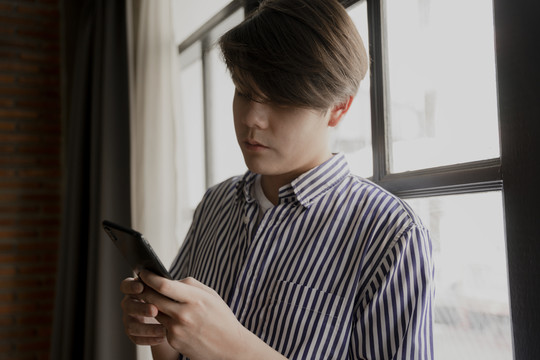 亚洲年轻人在窗口附近使用智能手机。