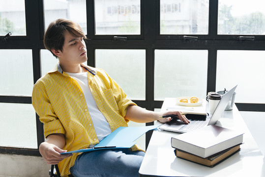 穿着黄衬衫的亚洲年轻人在现代办公室的办公桌旁工作。