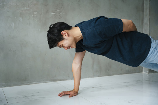侧视图-亚洲年轻男子在健身房单手做俯卧撑。