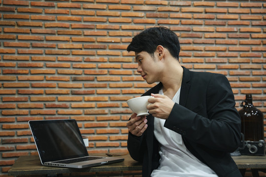 亚洲年轻商人喜欢在办公室里喝热咖啡，看笔记本电脑。