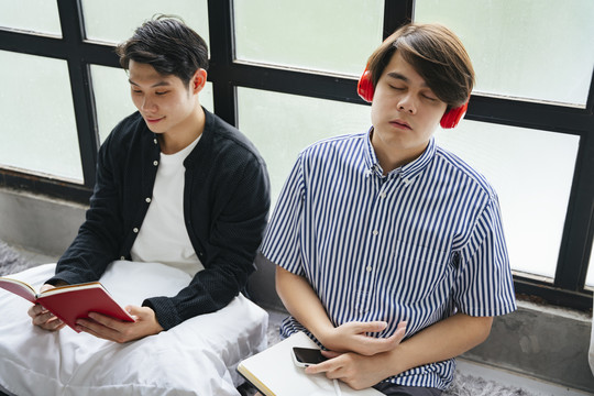 两名亚洲LGBTQ+男性在家共度时光。读书和听音乐。