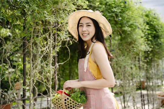 美丽的亚洲农妇戴着帽子，手里拿着装满蔬菜的篮子。