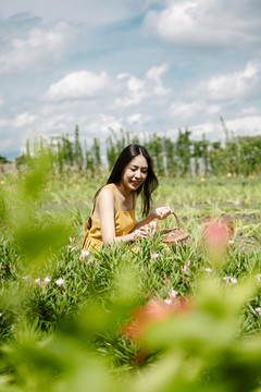 侧视图-身着黄色连衣裙的亚洲美女手持花篮在户外观赏鲜花。