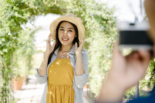 夏天，一位亚洲女游客戴着帽子在花园里用智能手机拍照。
