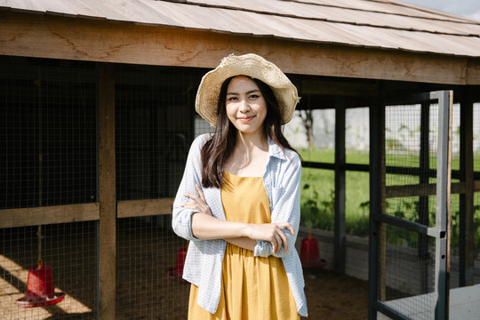 美丽的亚洲农妇戴着帽子站在农场的牲口棚前。