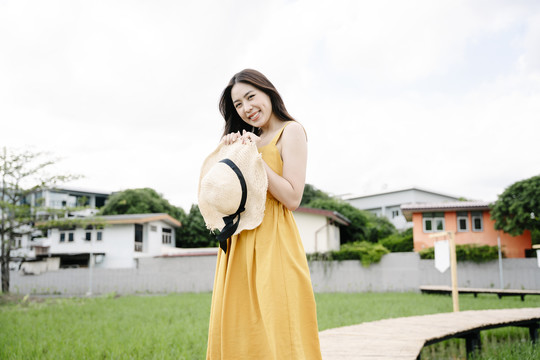 美丽的亚洲旅行家妇女手持帽子站在横跨稻田的木桥上的肖像。