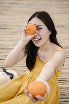 年轻亚洲女性的肖像，黑色头发，带橙色水果。健康生活理念。