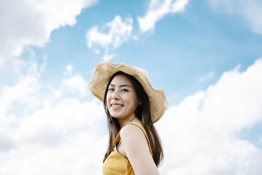 美丽的亚洲女旅行者戴着帽子，背景是夏天的云。