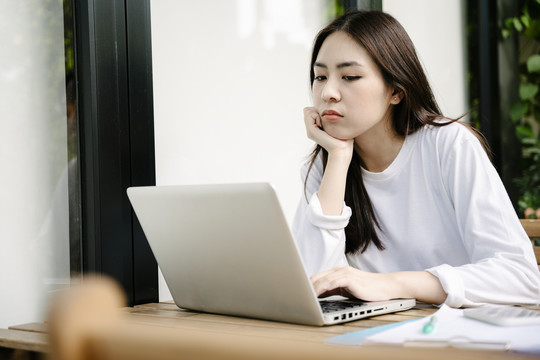 一个无聊的年轻女子坐在一起工作，手里拿着笔记本电脑，盯着电脑屏幕。