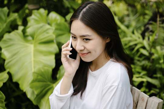 穿着白衬衫的亚洲美女在户外公园打电话。