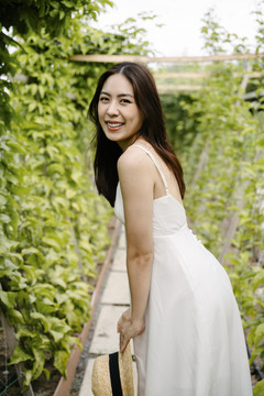 美丽的亚洲旅行家，穿着白色衣服，戴着帽子，在花园里玩得很开心。