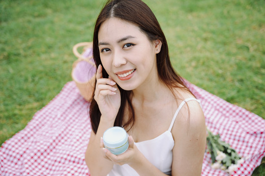 美丽的亚洲女人在户外用小罐子里的白色皮肤乳液。