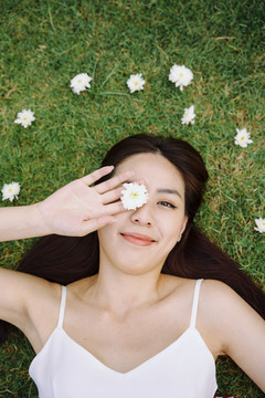 美丽的亚洲旅行家女子躺在草地上，身上开着白花。